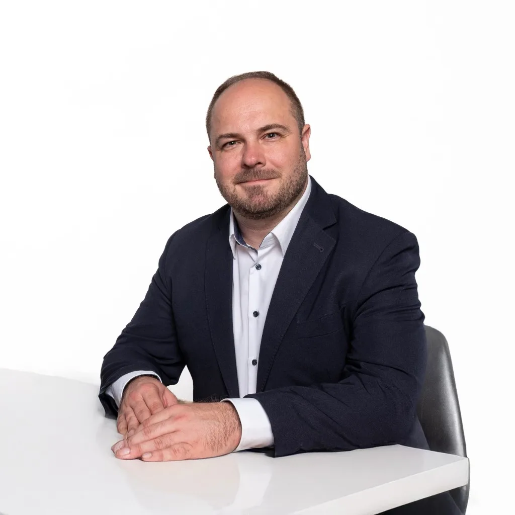 MUDr. Martin Knoz, Ph.D. seated at a desk in a navy blazer